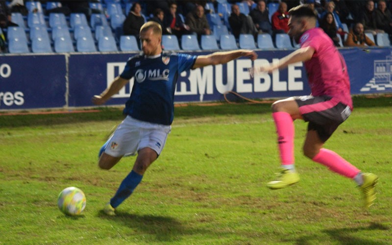 Un jugador del Linares centrando un balón ante la presión de un futbolista del antequera